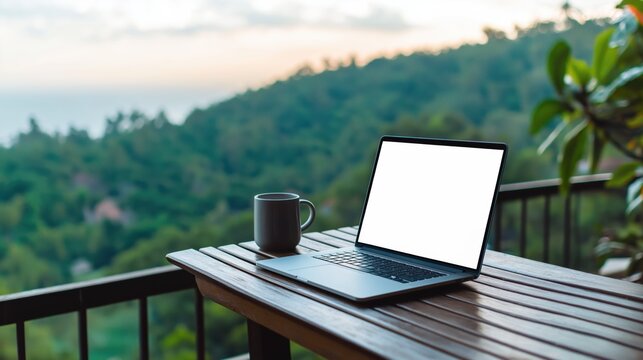 Laptop with blank screen beside a mug on a wooden table, offering a scenic view of lush tropical mountains