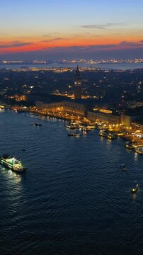 Drone footage captures illuminated Venice waterfront and historic buildings at dusk with calm sea and colorful sky.