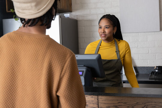 African American cashier and customer paying at cafe register, yellow top and apron, copy space