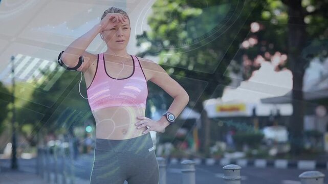 Female runner approaching bollards, slowing, tapping watch, adjusting armband, cooling down to rest