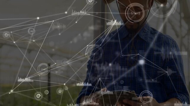 Tapping tablet, man wearing brimmed hat, denim shirt monitoring in greenhouse, with data overlay