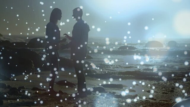 Woman offering object, man leaning in for film memento swap at backlit shore, bokeh obscuring hands