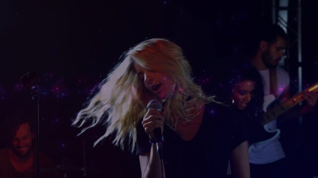 Singing lead singer holding wired mic on stage in black top, purple light effects with bass
