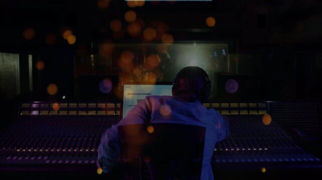 Audio engineer starting playback tweaking faders and balancing mix while orange bokeh filling frame