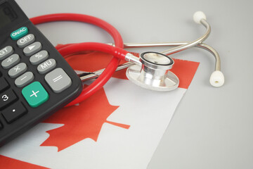 Red stethoscope and calculator on flag of Canada. Cost of Canadian medicine and health insurance...