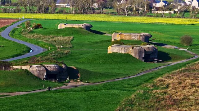 German coastal artillery bunkers at Longues-sur-Mer battery surrounded by green fields and paths in Normandy, aerial orbit