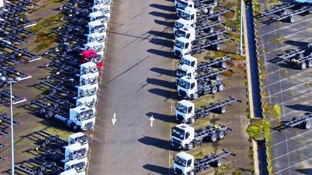 Slow aerial drone flyover reveals hundreds of white Renault cab-chassis trucks in organized rows with dramatic diagonal shadows at Gare A6 logistics depot in Gonfreville, France