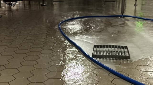 Wet tiled floor with cleaning hose in industrial setting at night