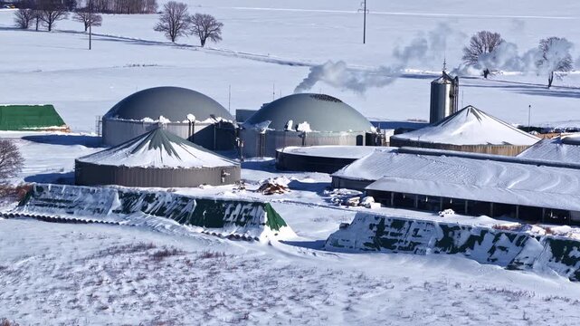Aerial parallax shot of biogas anaerobic digestion plant with large dome digesters, silos and silage piles covered in snow in Latvian winter countryside