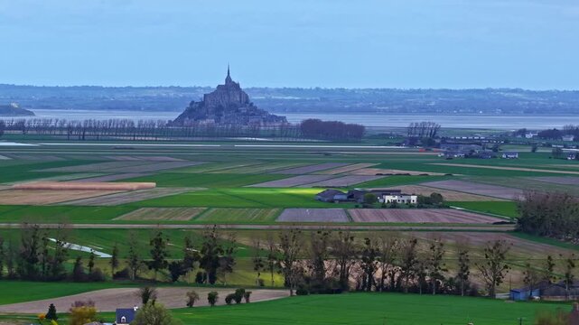 Mont Saint-Michel abbey rising from fields, historic landmark in France, aerial view
