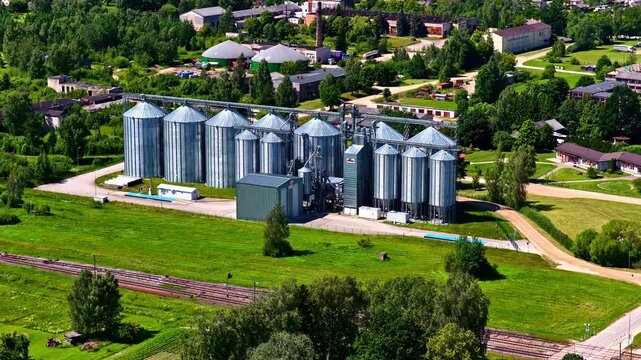 An aerial view of a row of silver grain silos in a green field