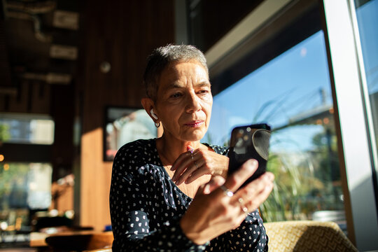 Mature woman video calling on smartphone at cafe window