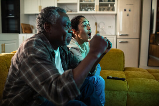 Older man and woman cheering while watching sports on television at home