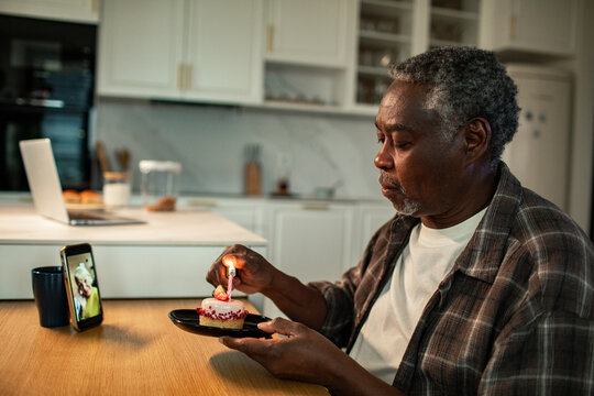 Senior man lighting birthday candle during video call in home kitchen