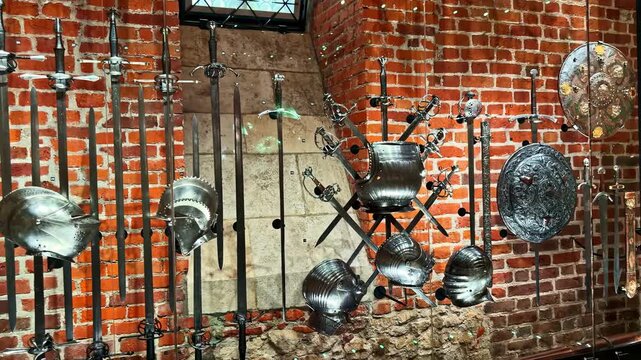 Display of historic swords, helmets, and armor in the armory of Wawel Royal Castle museum in Krakow, Poland
