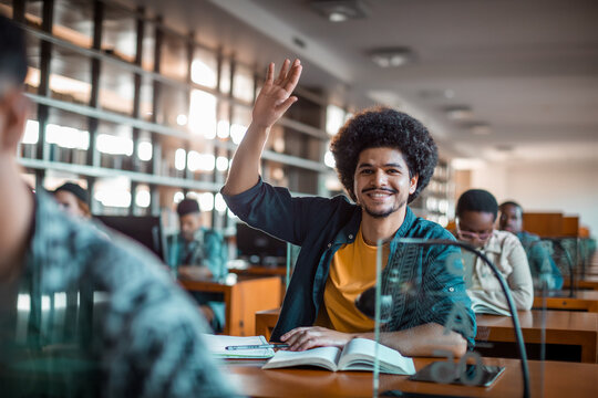 Smiling college student raising hand in library classroom