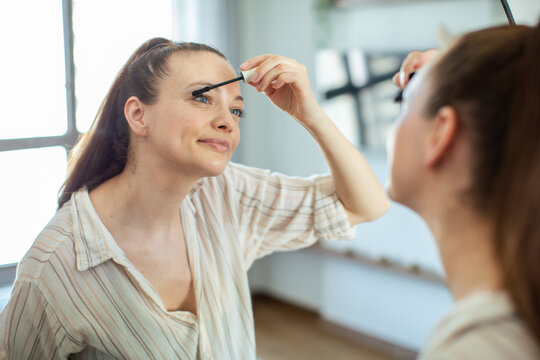 Smiling woman applying mascara in a home mirror