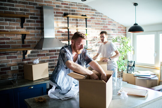 Two men unpacking moving boxes in modern kitchen