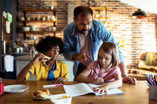 Father helping children with homework at kitchen table