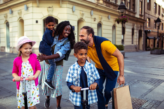 Cheerful family with children riding scooters on city street