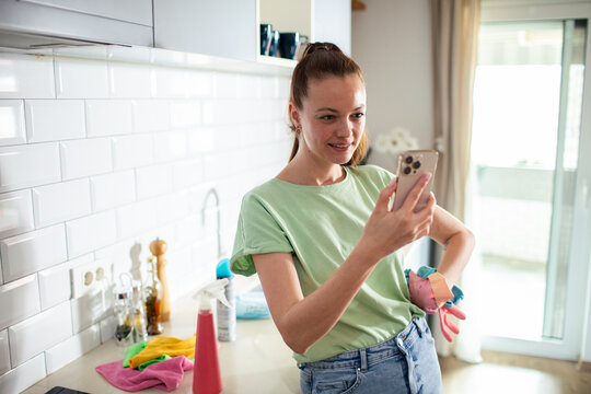 Young woman video chatting while cleaning kitchen at home