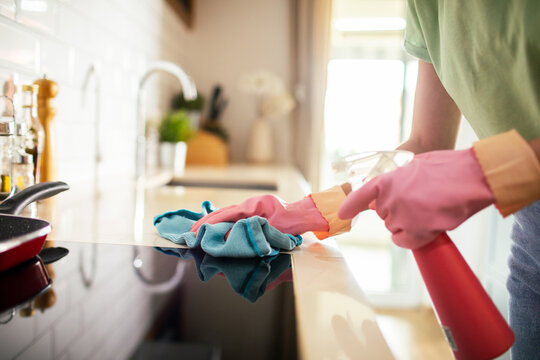 Gloved hands cleaning kitchen stovetop with spray bottle