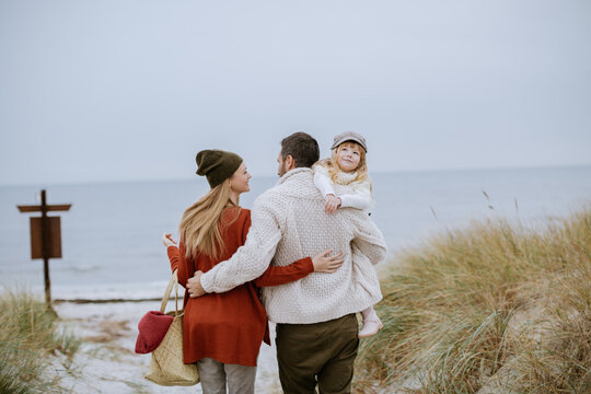 Parents carrying daughter along winter beach dunes