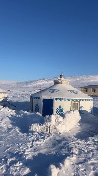 Authentic vertical footage showing traditional gers (yurts) on a wind-swept snowy plateau. Faint horse tracks are visible in the snow nearby.