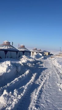 Atmospheric vertical shot of a lonely traditional yurt in winter. The cold blue snow contrasts with a warm light glowing from the doorway at dawn.