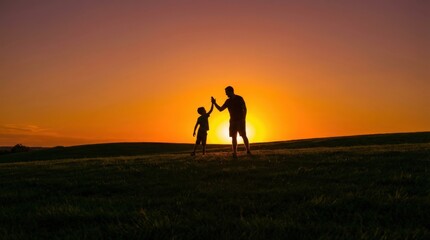 Fototapeta premium Father and young son sharing a high five in silhouette against a vibrant golden sunset