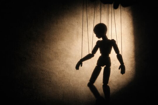 Silhouette of a marionette puppet casting shadow on wall