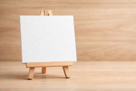 Close up white canvas on a small easel with a light wooden background and copy space