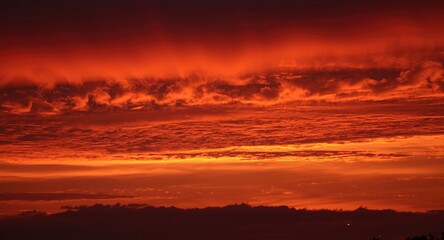Fototapeta premium Vivid crimson and tangerine sunset sky casting shadows on clouds