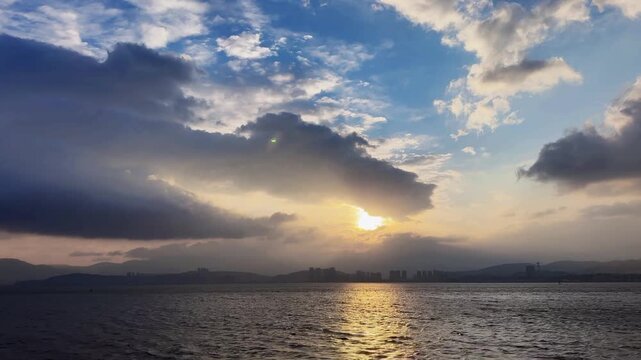 Mesmerizing horizontal footage capturing the warm golden light of a large sun as it dips toward the hazy horizon over a rhythmic sea with a glittering reflection path.