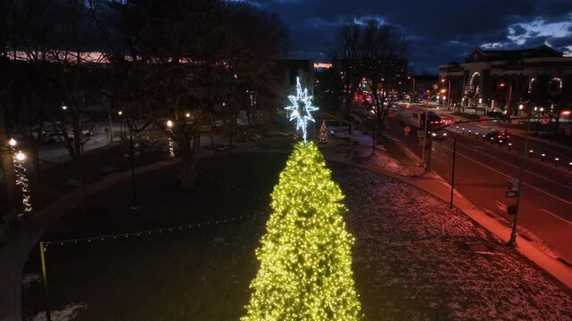 Aerial drone descent over illuminated Christmas tree and street traffic in Hershey, Pennsylvania, with festive lights and dramatic twilight sky during winter Christmas season evening atmosphere in USA