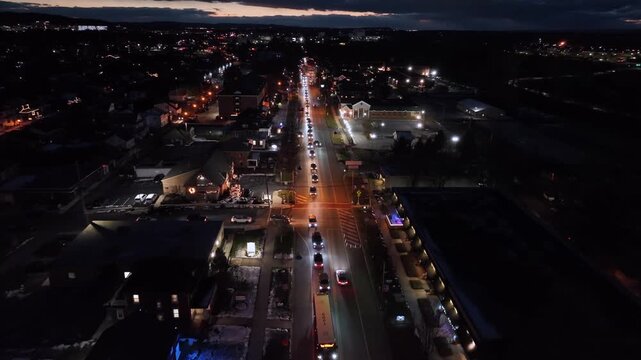Aerial view of busy road in small American city at night during winter with light snowfall, traffic and festive Christmas decorations creating vibrant holiday atmosphere in the United States