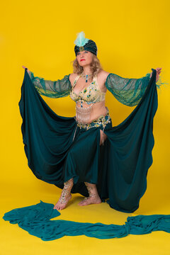 Mature adult female exotic dancer dressing in green eastern dancing stage costume - turban, bra top, long skirt and she is not wearing any footwear, walkdown, performing full length yellow background
