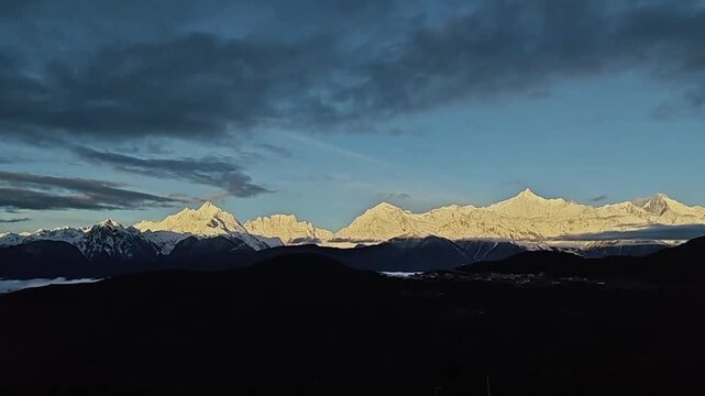 Breathtaking wide horizontal view of the thirteen peaks of Meili Snow Mountain turning gold during a clear spring morning sunrise.
