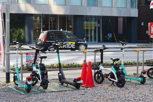 TOKYO, JAPAN - December 28, 2025: Rental Luup e-bikes and a Luup e-scooter in a car park in Tokyo's Nihonbashi area. A taxi is passing in the background.