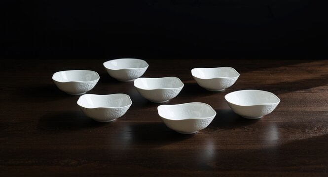 White bowl set of eight featuring multiple shapes and intricate textures showcased on a dark table setting background