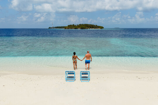 Couple walking hand in hand to the sea on a beach in the Maldives