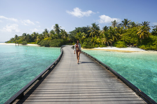 Young asian woman in bikini walking on jetty on an island in the Maldives