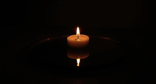 Tight frame of a candle flame doubling on a dark shiny mirror with a thoughtful atmosphere