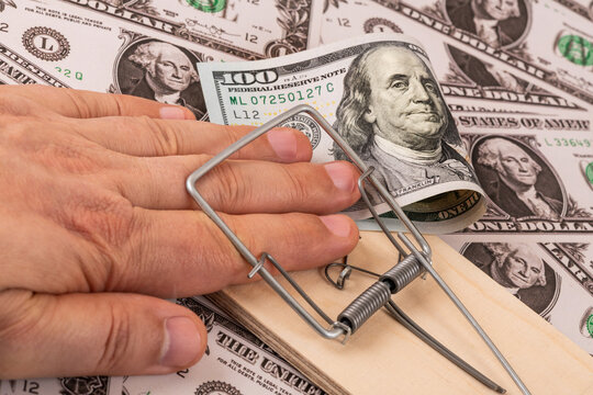A hand in a mousetrap and a $100 bill against a background of $1 bills