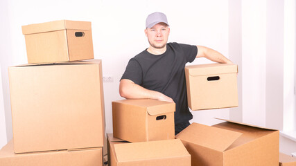 Fototapeta premium A construction worker, holding a cardboard box, stands in front of a gray background. In the background, we can see cardboard boxes filled with furniture, which are typical of an office during a move