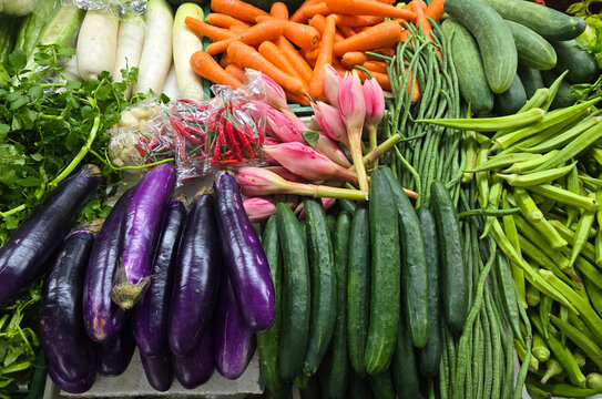 A high angle view of various fresh vegetables including eggplants, cucumbers, carrots, okra, long beans, and pink torch ginger flowers "bunga kantan" at a local wet market.
