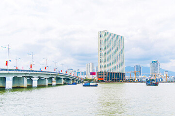 Cai River with fishing boats and a bridge in Nha Trang city on a cloudy day. Panorama view of skyscrapers in Nha Trang in Vietnam