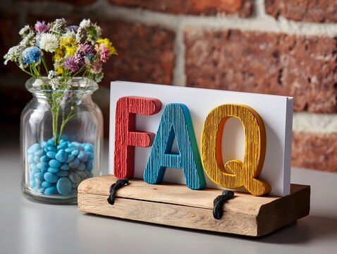 木製スタンドに置かれたカラフルなFAQの文字と瓶に生けられた花や石の背景素材