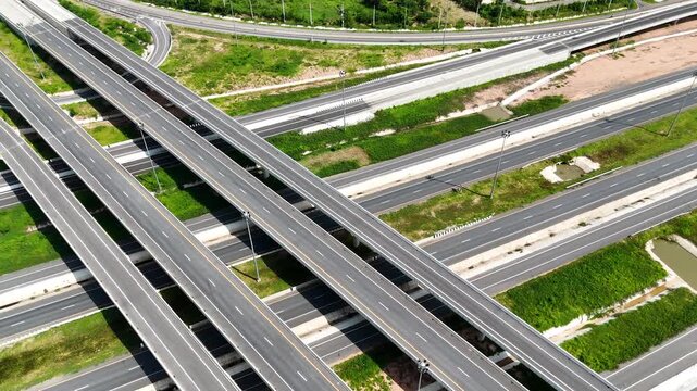 Aerial view of modern highway interchange with multilayer roads and curved ramps surrounded by green farmland, showcasing transportation infrastructure, urban development, and road network planning.