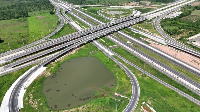 Aerial view of modern highway interchange with multilayer roads and curved ramps surrounded by green farmland, showcasing transportation infrastructure, urban development, and road network planning.
